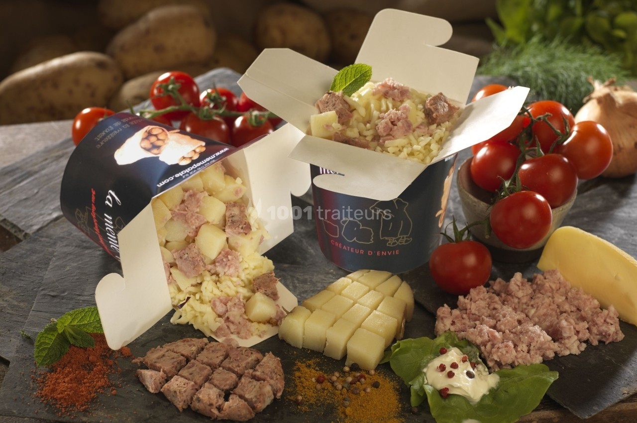 Deux boîtes ouvertes contenant un plat de pommes de terre, fromage et viande hachée, entourées d'ingrédients frais.