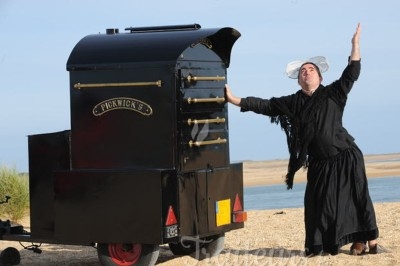 Un homme en tenue traditionnelle pose de manière théâtrale près d'un four mobile sur une plage.