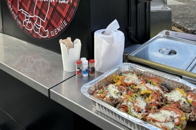 Plateau en aluminium contenant un plat cuisiné avec légumes, viande et fromage, posé sur un comptoir de food truck.