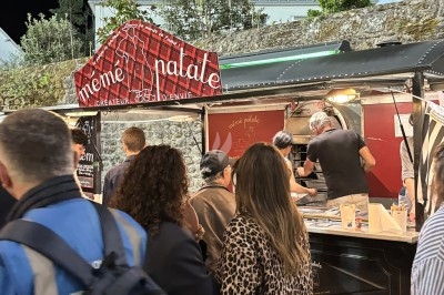 File d'attente devant un food truck avec des clients commandant et un cuisinier préparant des plats.