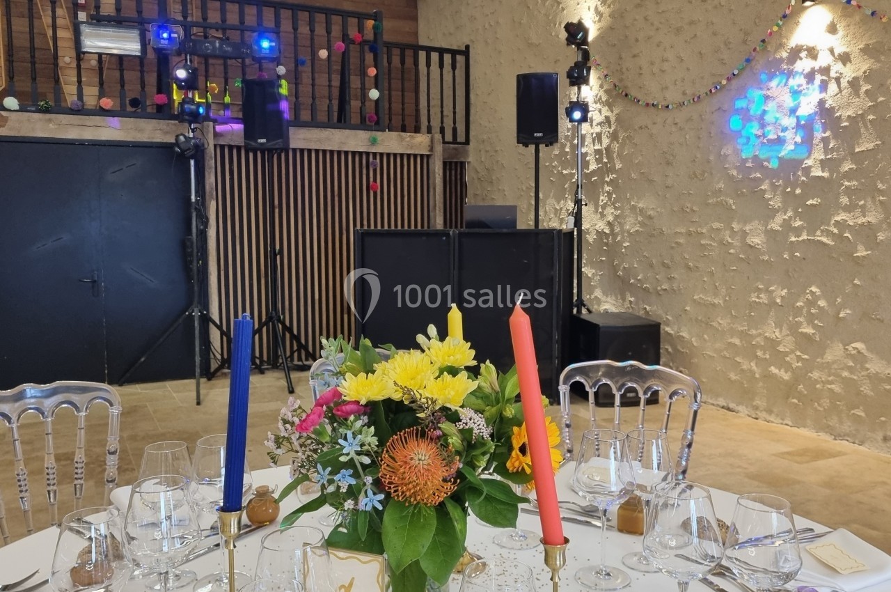 Salle de réception décorée avec des guirlandes lumineuses, une table dressée avec des fleurs et des bougies colorées.