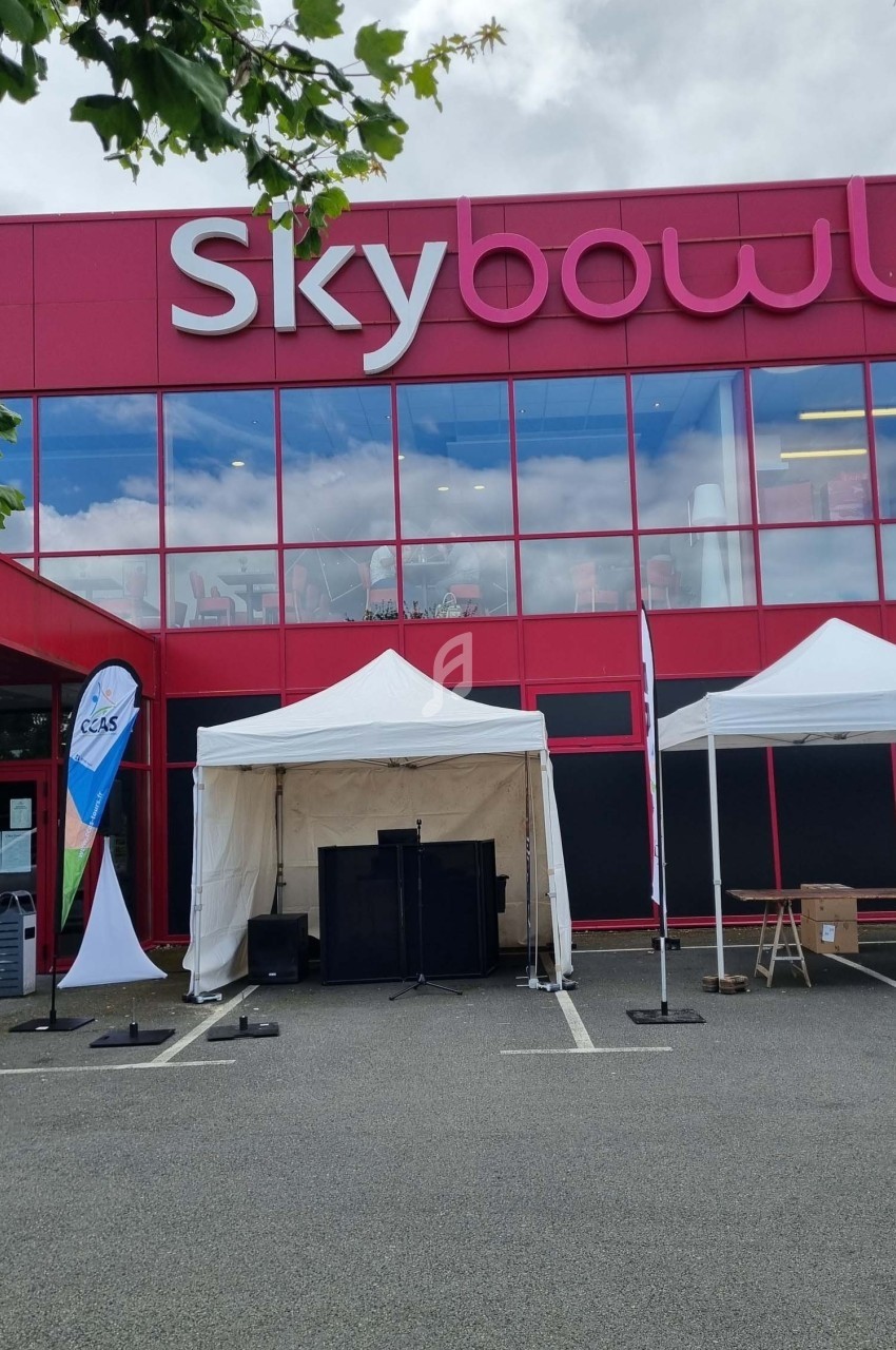 Façade rouge d'un bâtiment nommé ’Skybowl’ avec des tentes blanches installées sur le parking devant.
