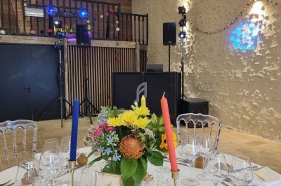 Table décorée avec des fleurs colorées et bougies, dans une salle avec piste de danse et éclairages festifs.