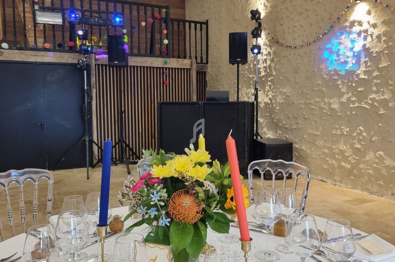 Table décorée avec des fleurs colorées et bougies, dans une salle avec piste de danse et éclairages festifs.