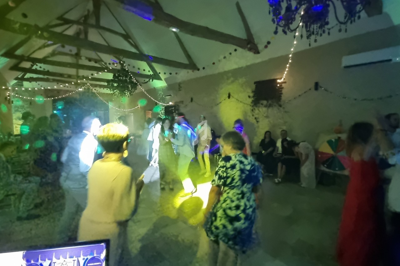 Des personnes dansent dans une salle décorée avec des guirlandes lumineuses et des jeux de lumière colorés.