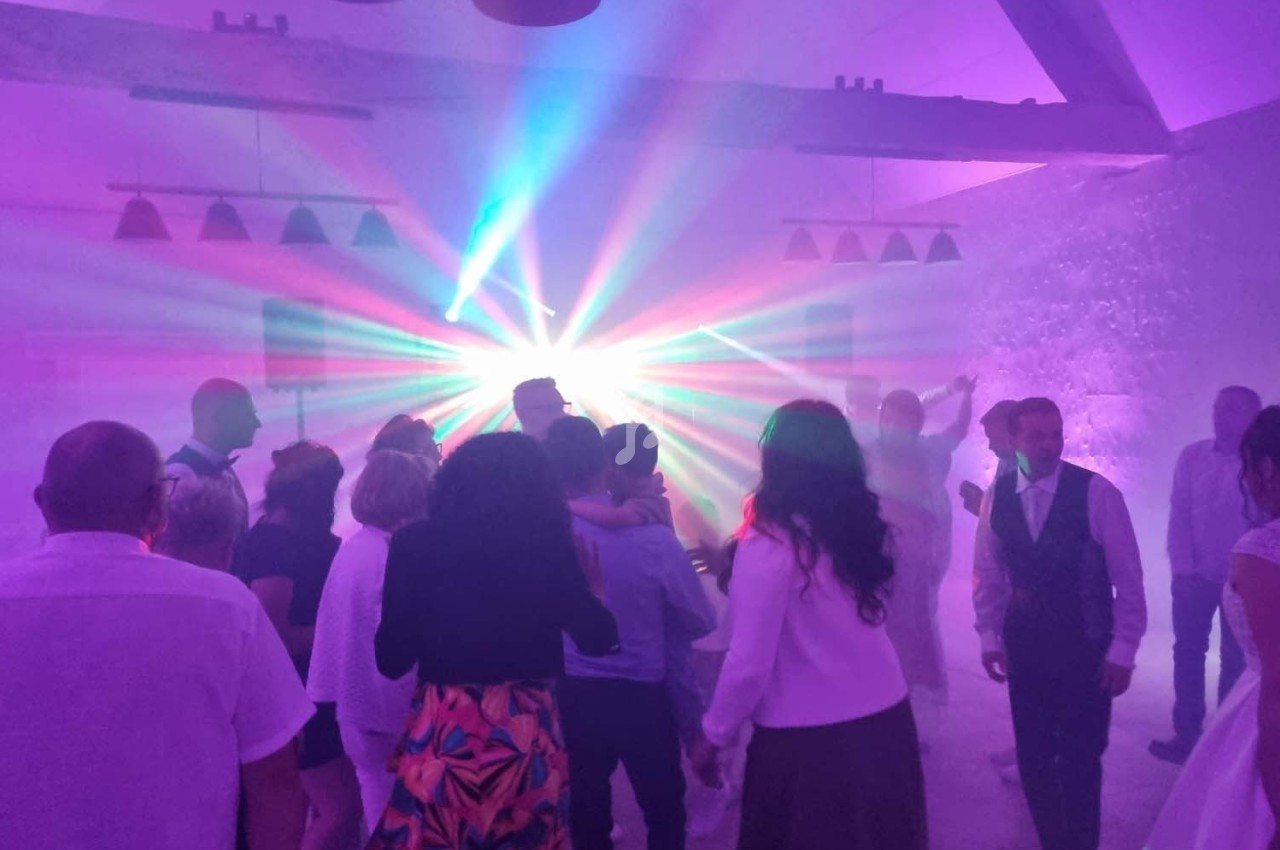 Groupe de personnes dansant sous des lumières colorées dans une ambiance festive en intérieur.