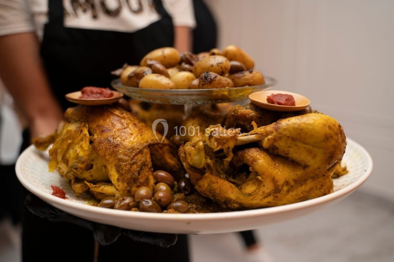 Poulet rôti épicé servi avec pommes de terre, olives et garniture de sauce rouge sur un plat blanc.