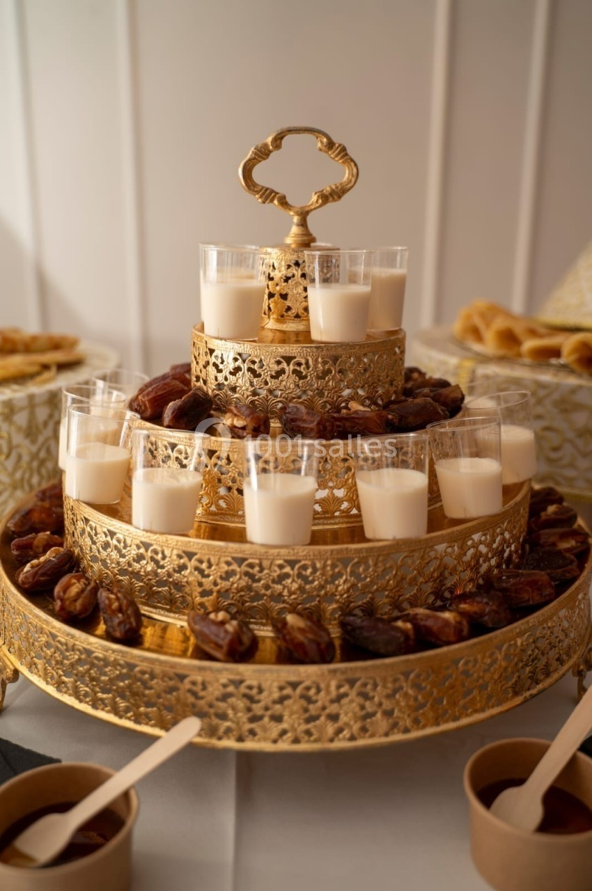 Plateau doré à étages décoré de dattes et de verrines de lait, disposé sur une table blanche.