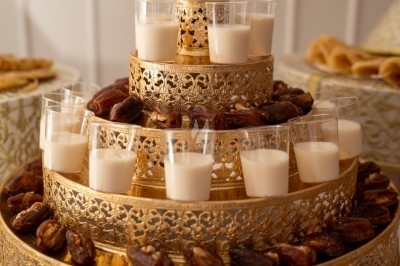 Plateau doré à étages décoré de dattes et de verrines de lait, disposé sur une table blanche.
