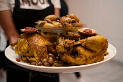 Poulet rôti épicé servi avec pommes de terre, olives et garniture de sauce rouge sur un grand plat.