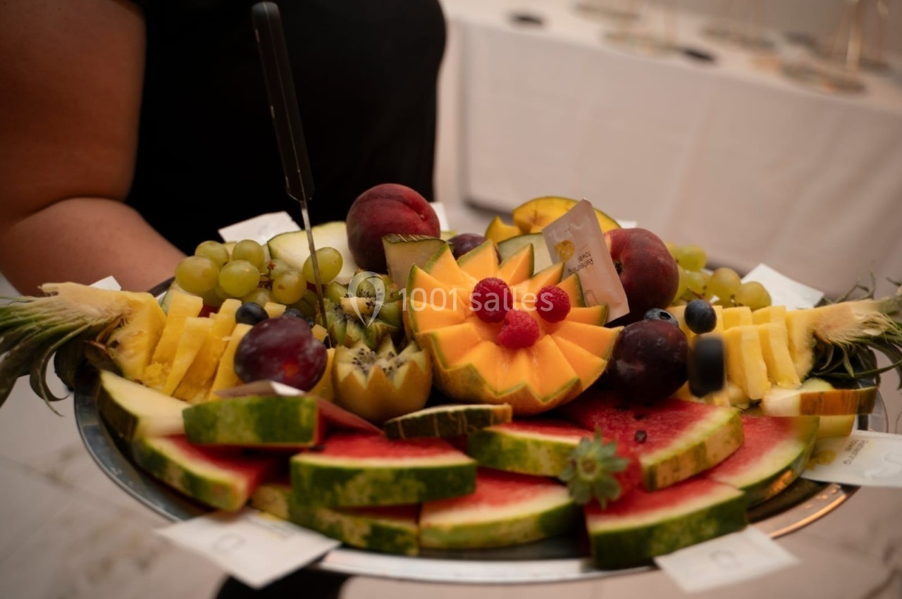 Plateau de fruits variés comprenant pastèque, ananas, kiwi, raisins, pêches et baies, présenté sur une table.