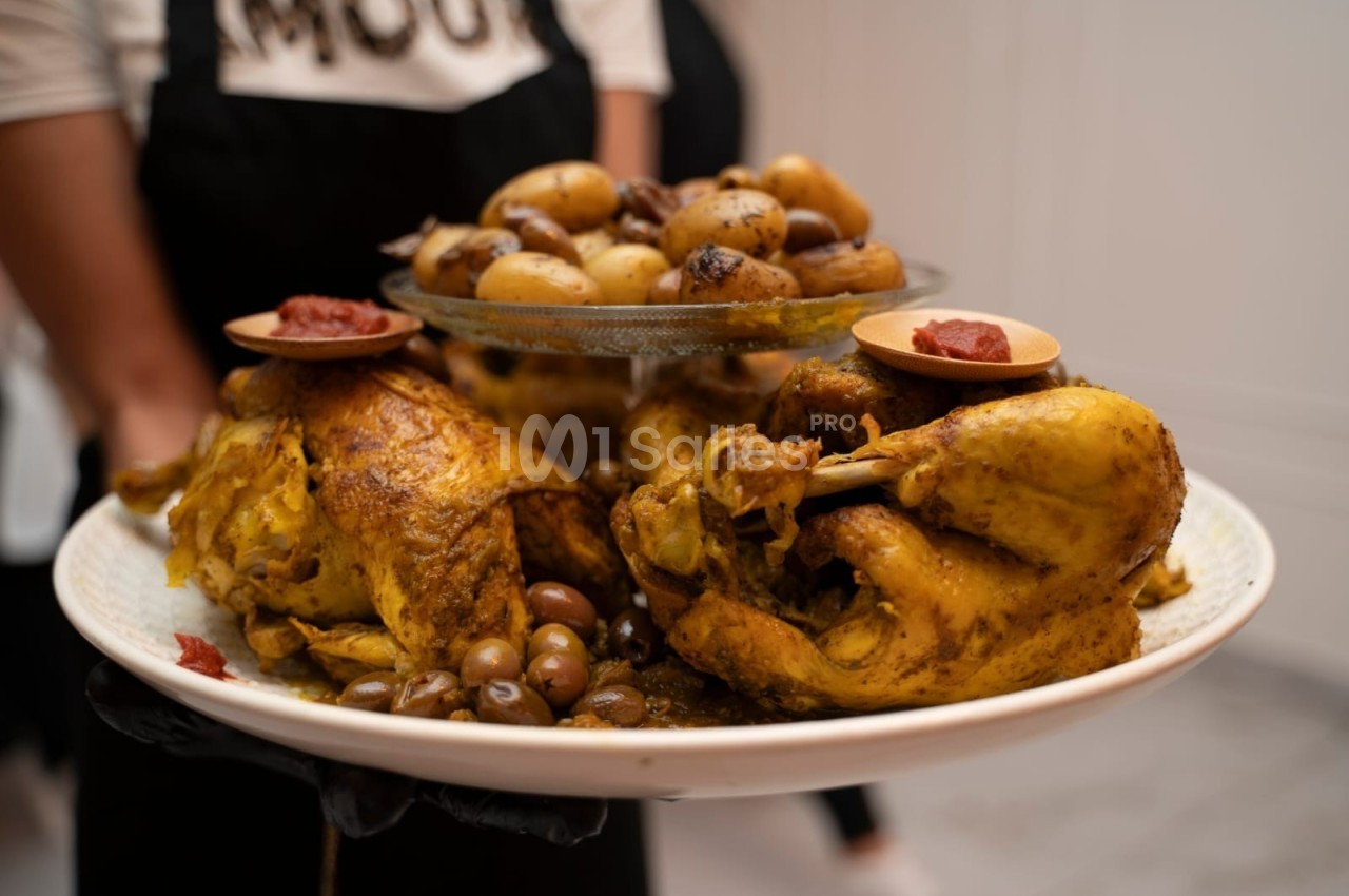 Poulet rôti épicé servi avec pommes de terre, olives et garniture de sauce rouge sur un plat blanc.