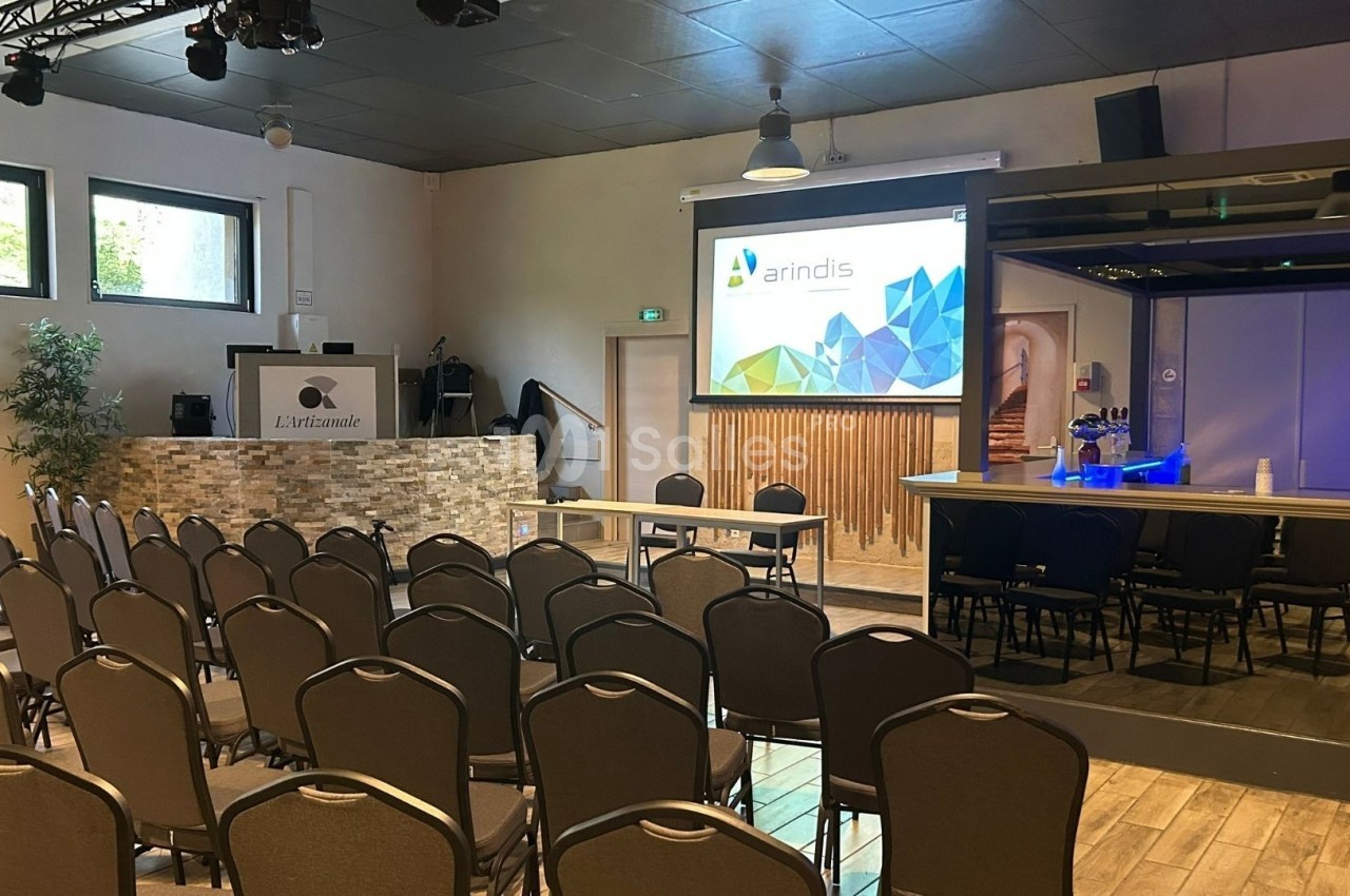 Salle de conférence équipée de chaises, d'un écran de projection, d'un pupitre et d'un bar en arrière-plan.