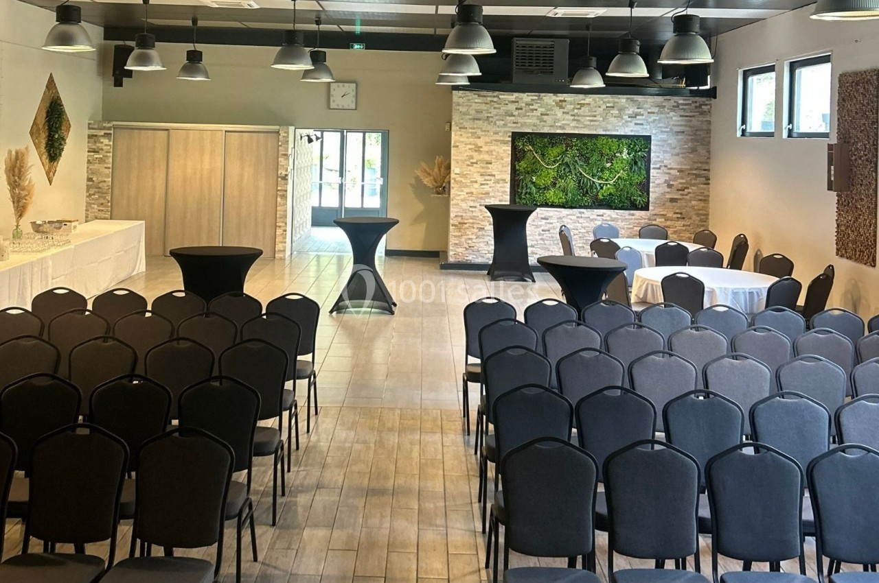 Salle de conférence aménagée avec des rangées de chaises, des tables hautes et une décoration murale végétale.