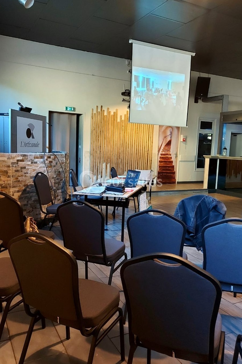 Salle de conférence avec chaises vides, écran de projection allumé et table équipée d'un ordinateur portable.