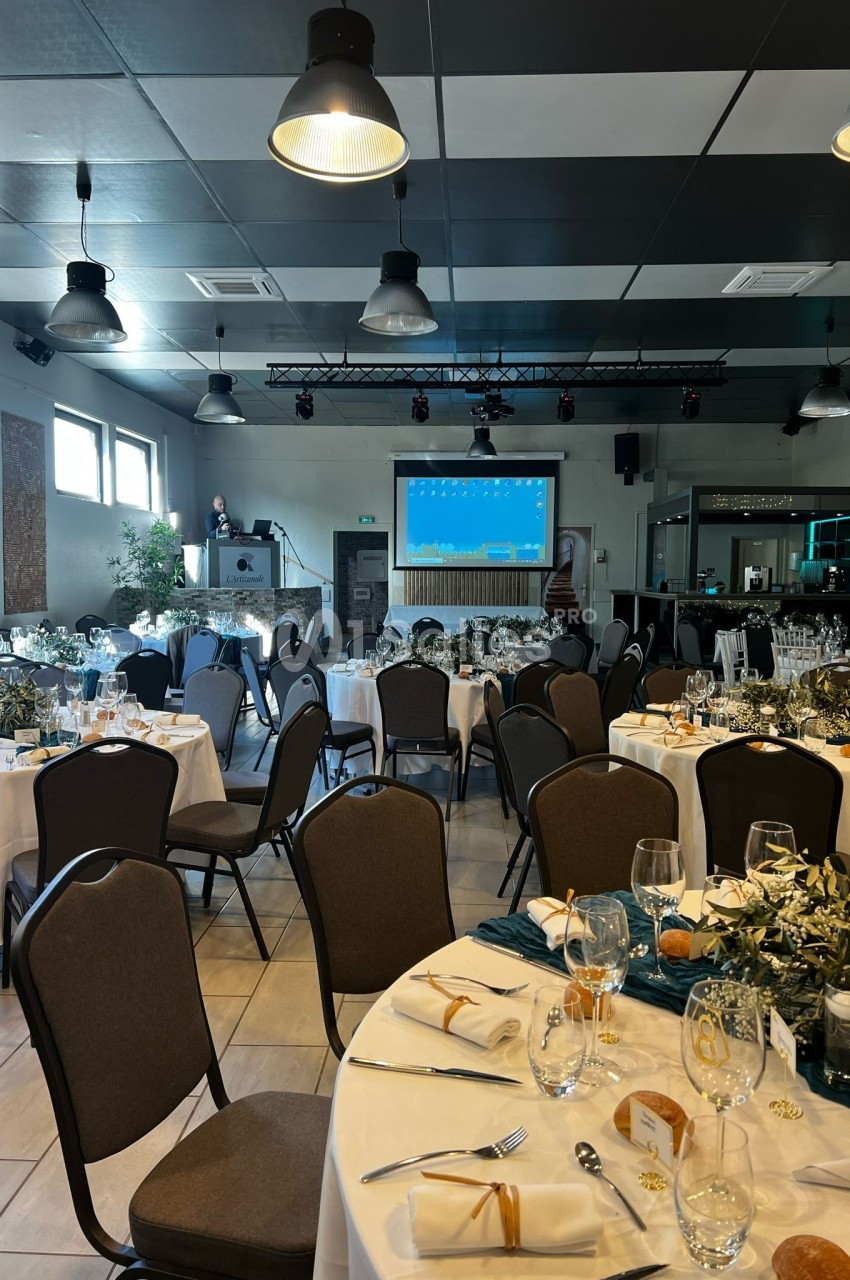 Salle de réception décorée avec des tables dressées, des chaises alignées et un écran de présentation en arrière-plan.