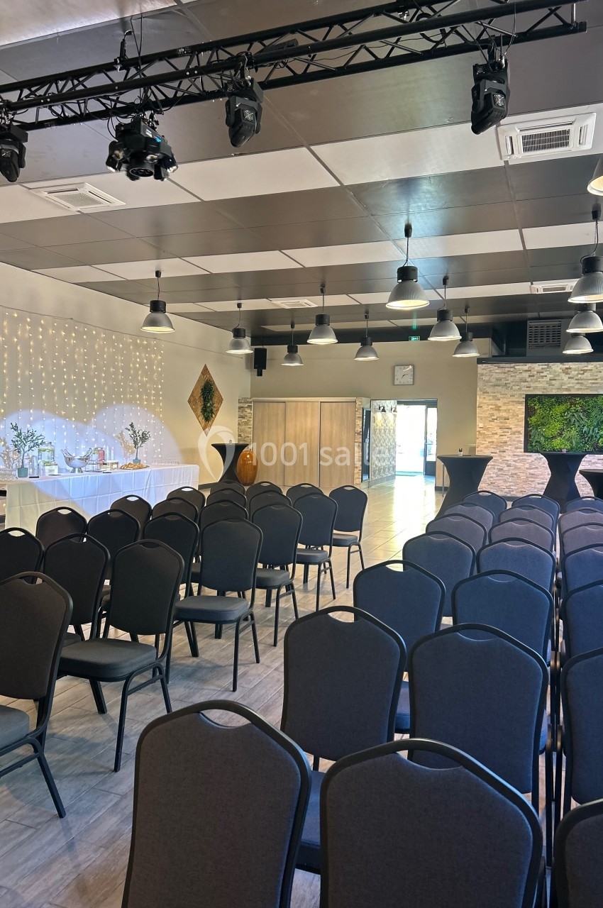 Salle de réception avec rangées de chaises, tables décorées, éclairage suspendu et murs en pierre.