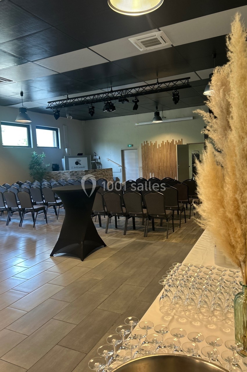 Salle de réception aménagée avec des rangées de chaises, une table de verres et une décoration de pampas au premier plan.
