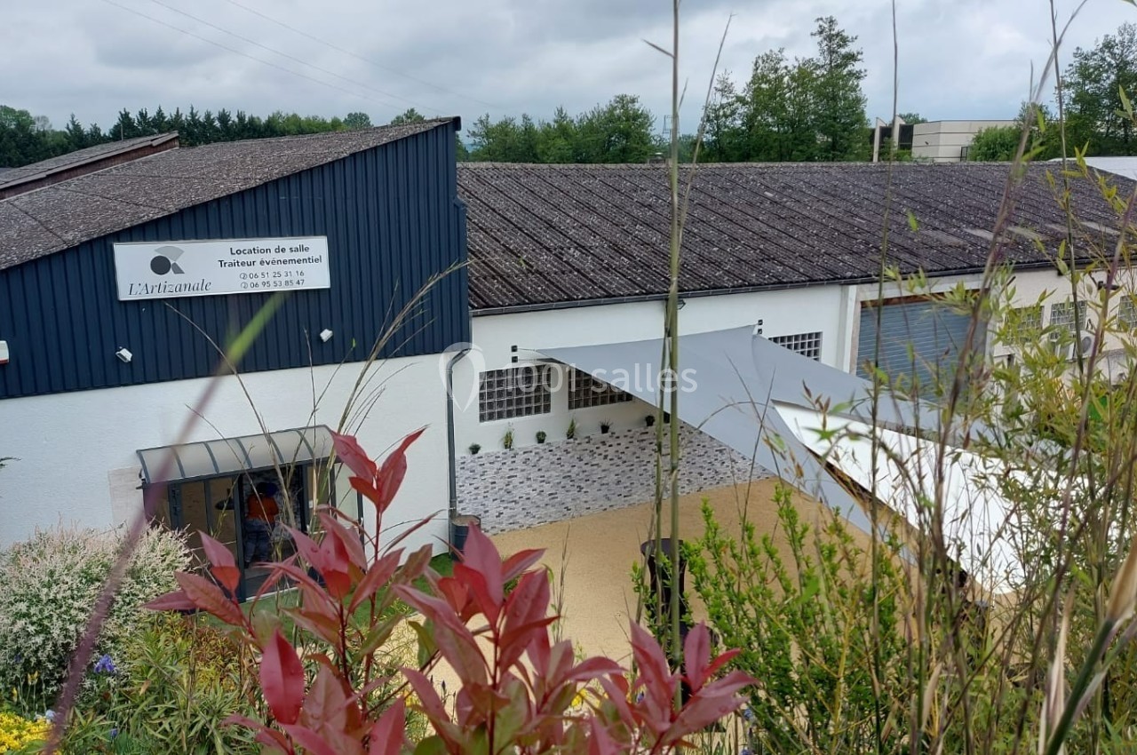 Bâtiment avec toit en tuiles, façade blanche, enseigne visible et espace extérieur aménagé avec végétation.