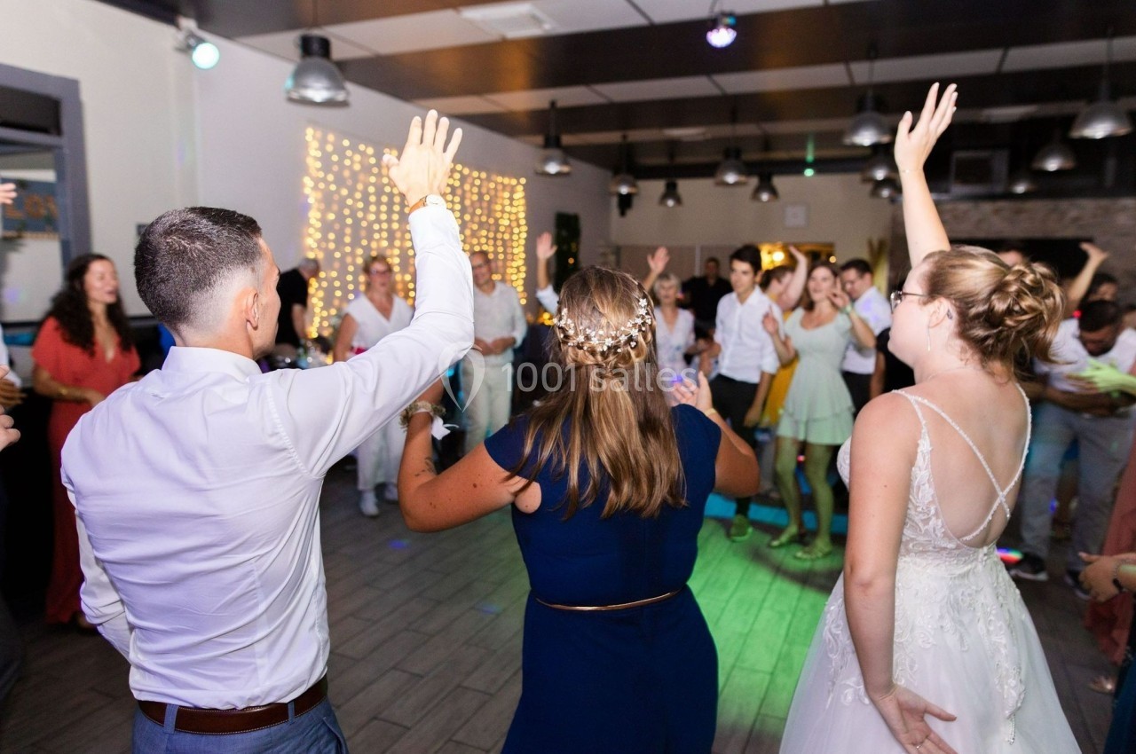 Des personnes dansent et lèvent les bras lors d'une fête dans une salle éclairée avec des guirlandes lumineuses.