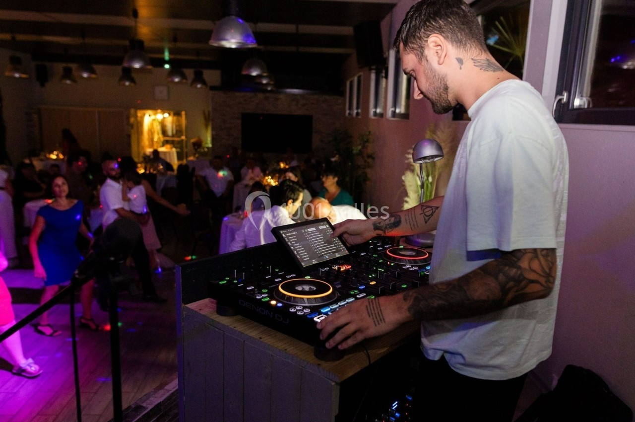 Un DJ mixe de la musique sur une console dans une salle animée avec des invités dansant et discutant.