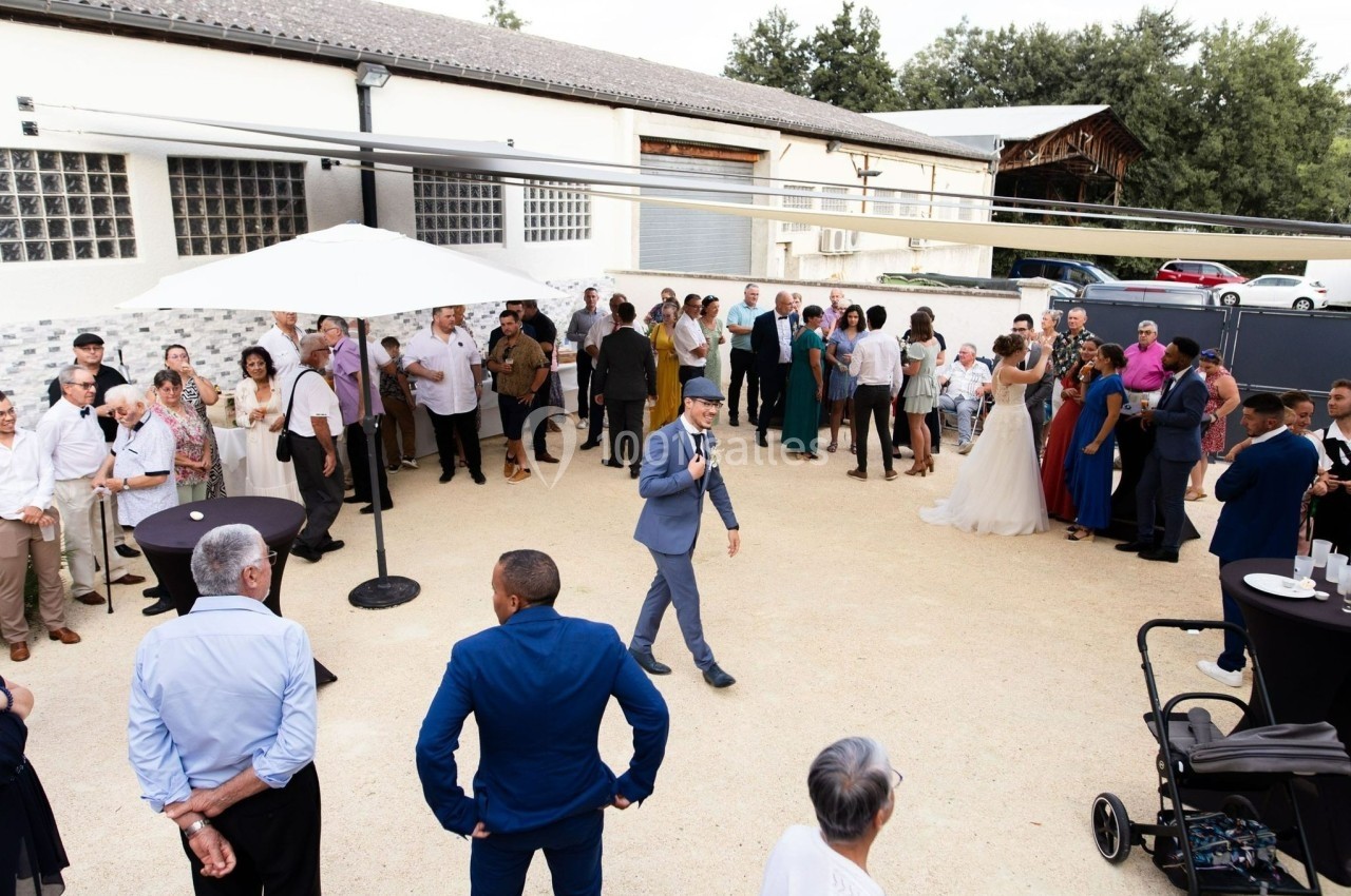 Groupe de personnes rassemblées en extérieur lors d'un événement, avec un homme en costume tenant un micro au centre.