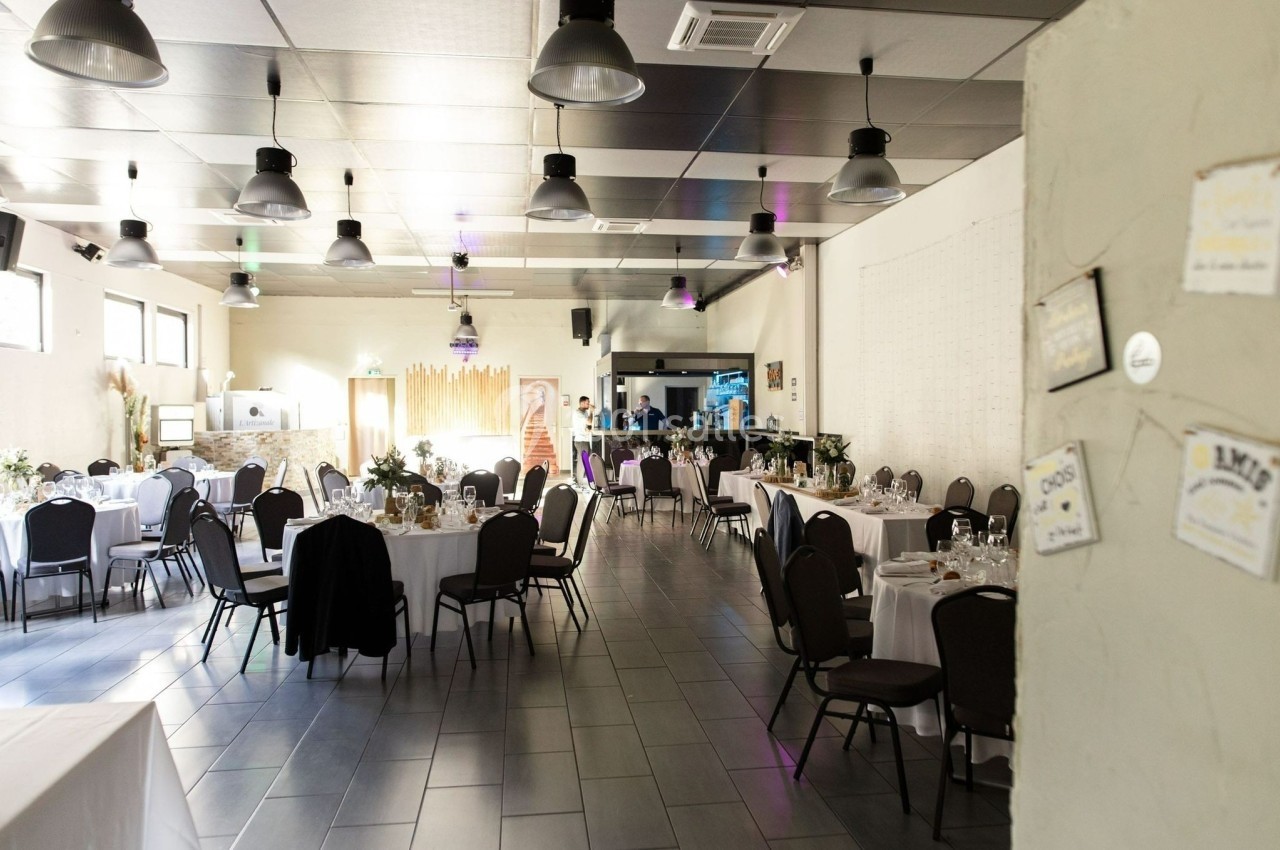 Salle de réception lumineuse avec tables rondes dressées, chaises noires et décorations sobres.