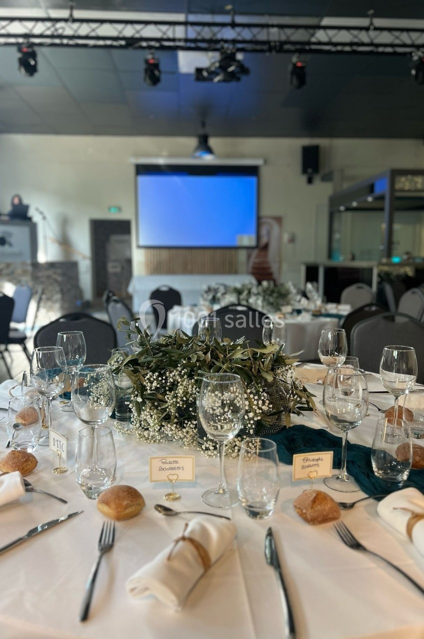 Table élégamment dressée avec nappes blanches, verres, couverts, petits pains et centre de table floral dans une salle de…