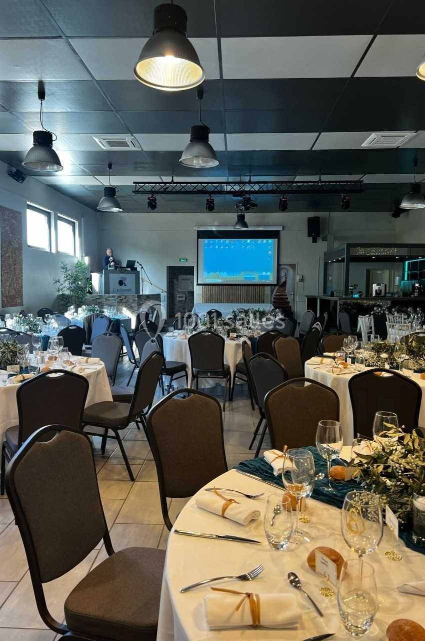 Salle de réception décorée avec des tables dressées, un écran de projection et un pupitre en arrière-plan.