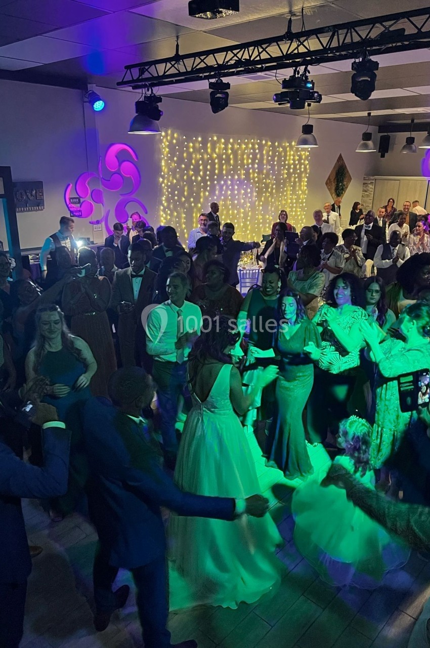 Groupe de personnes dansant lors d'une fête en intérieur, éclairée par des lumières colorées et une décoration lumineuse.