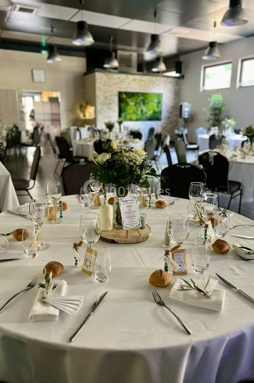 Salle de réception décorée pour un mariage, avec tables dressées, centres de table floraux et lumière naturelle.