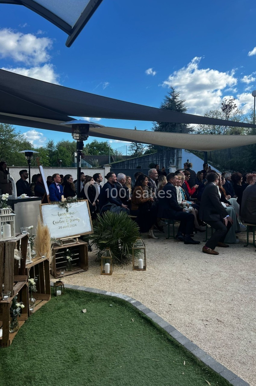 Groupe de personnes assises en extérieur sous des voiles d'ombrage, lors d'un événement par temps ensoleillé.