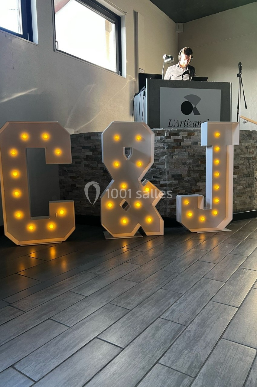 Lettres lumineuses ’C & J’ posées sur un sol en bois devant un pupitre dans une salle éclairée par la lumière naturelle.