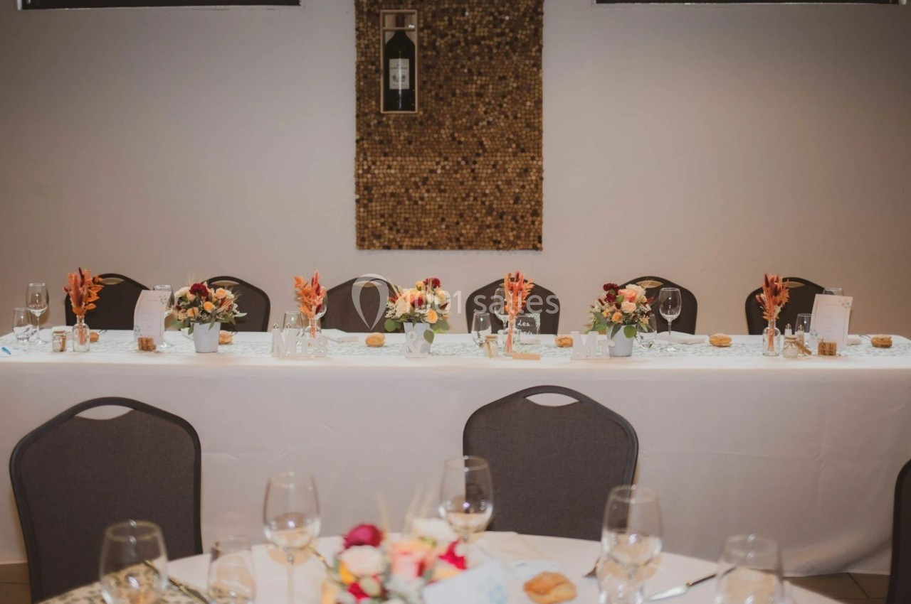 Table décorée pour un événement avec nappes blanches, fleurs colorées, verres et assiettes dans une salle sobre.