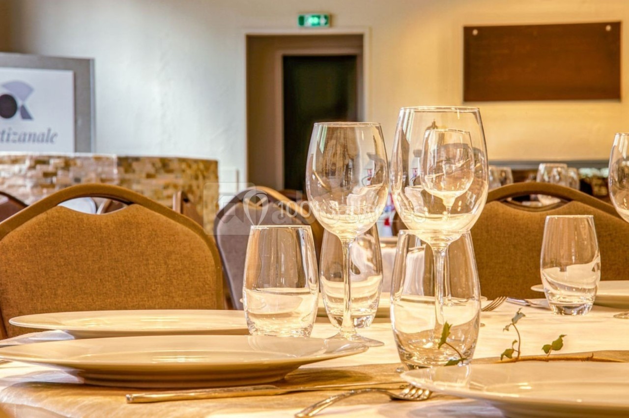 Salle de restaurant élégante avec tables dressées, verres et assiettes, ambiance lumineuse et chaleureuse.