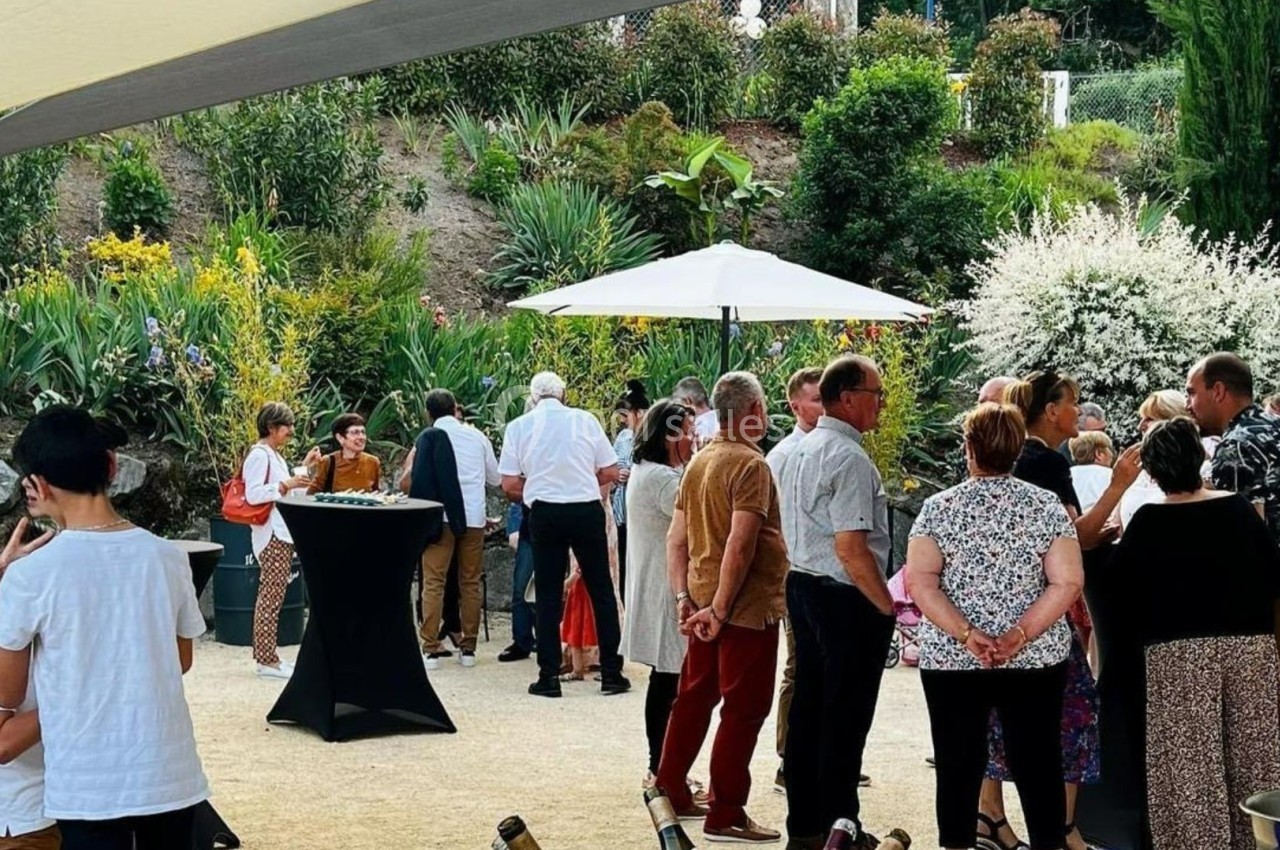 Groupe de personnes discutant dans un jardin aménagé avec des plantes, sous un parasol et par temps ensoleillé.