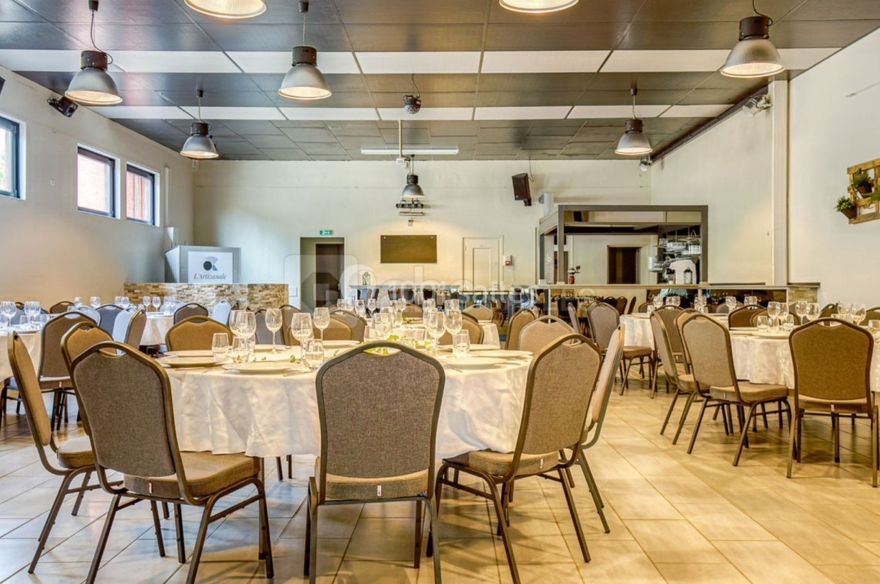 Salle de réception lumineuse avec tables rondes dressées, chaises grises et décor sobre.