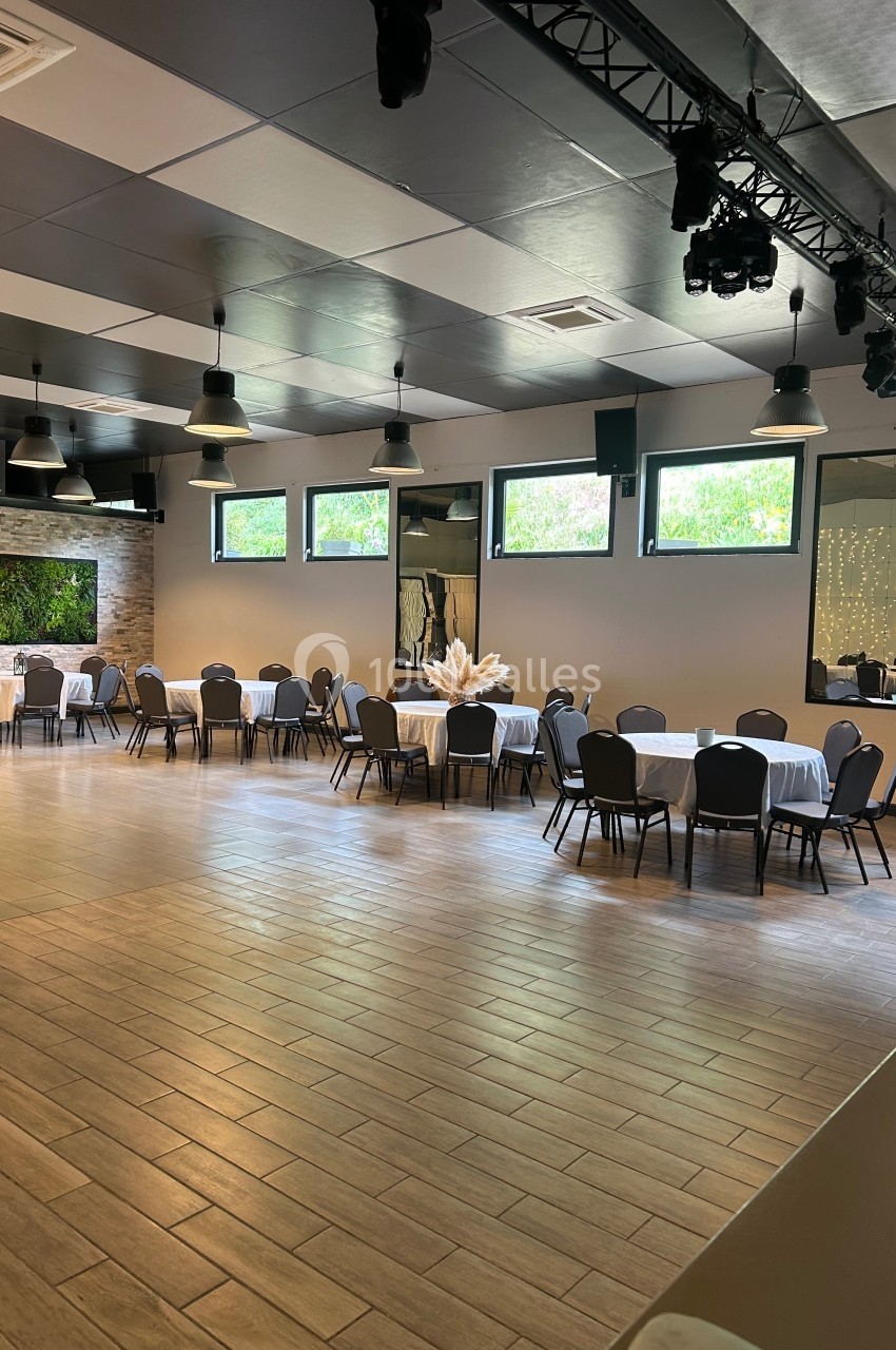 Salle de réception lumineuse avec tables rondes dressées, chaises noires et décoration murale végétale.
