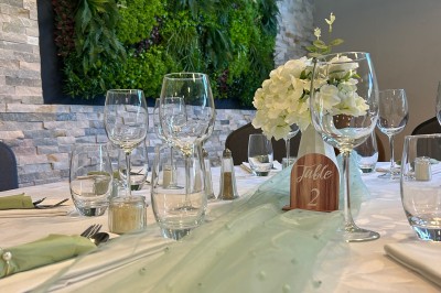 Table de réception décorée avec nappes blanches, verres, couverts, centres de table végétaux et guirlandes lumineuses en…