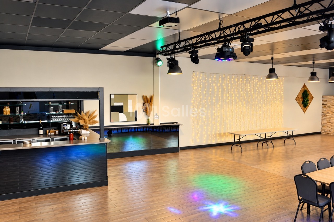 Salle de réception vide avec bar en angle à gauche, rideau lumineux blanc chaud au mur du fond, plafond à structure métallique portant des projecteurs et plusieurs chaises empilées à droite. Hmm, I should check: "plusieurs chaises empilées" is wrong