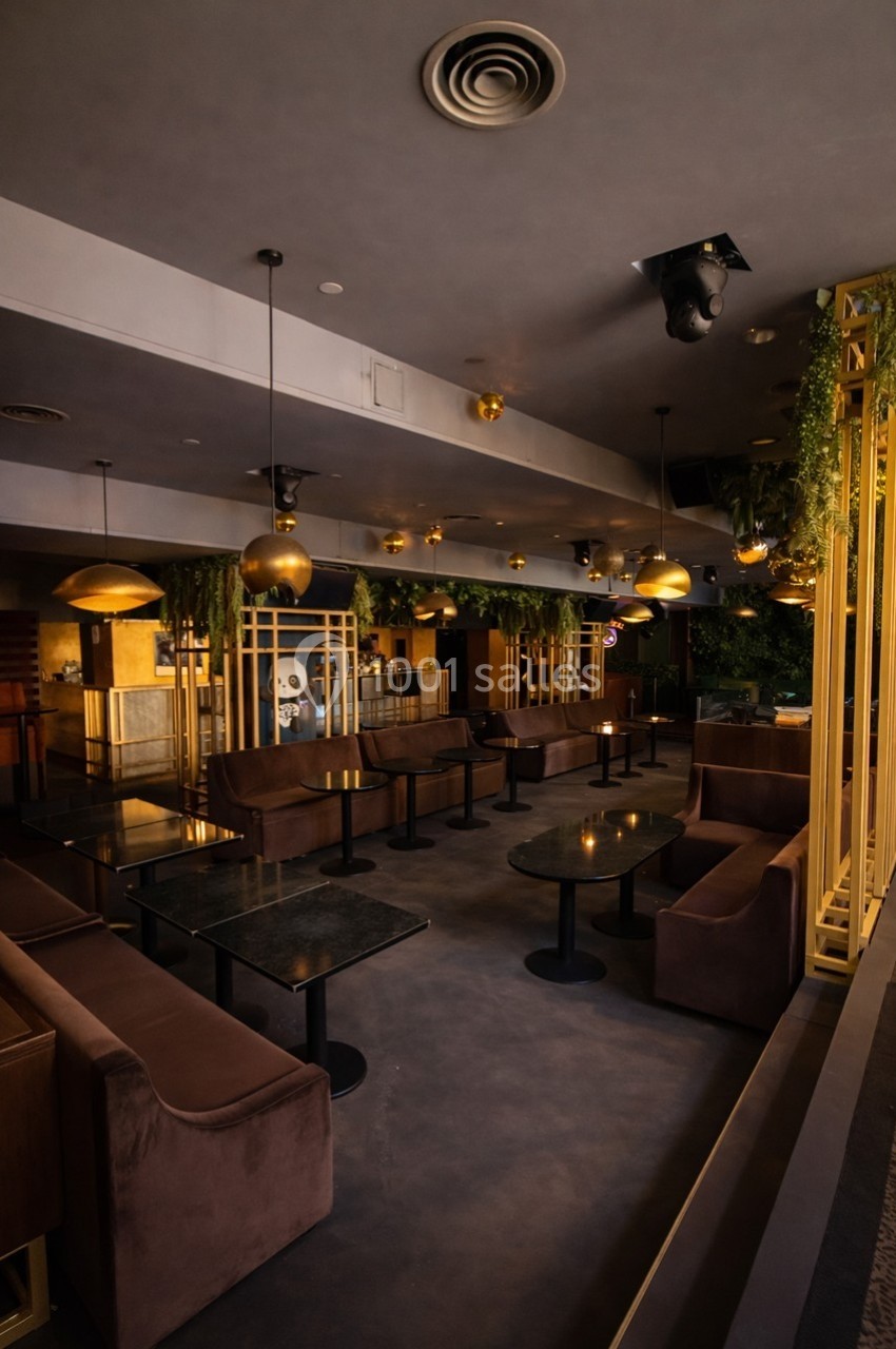 Salle de restaurant moderne avec tables en marbre, banquettes en velours et décoration végétale suspendue.