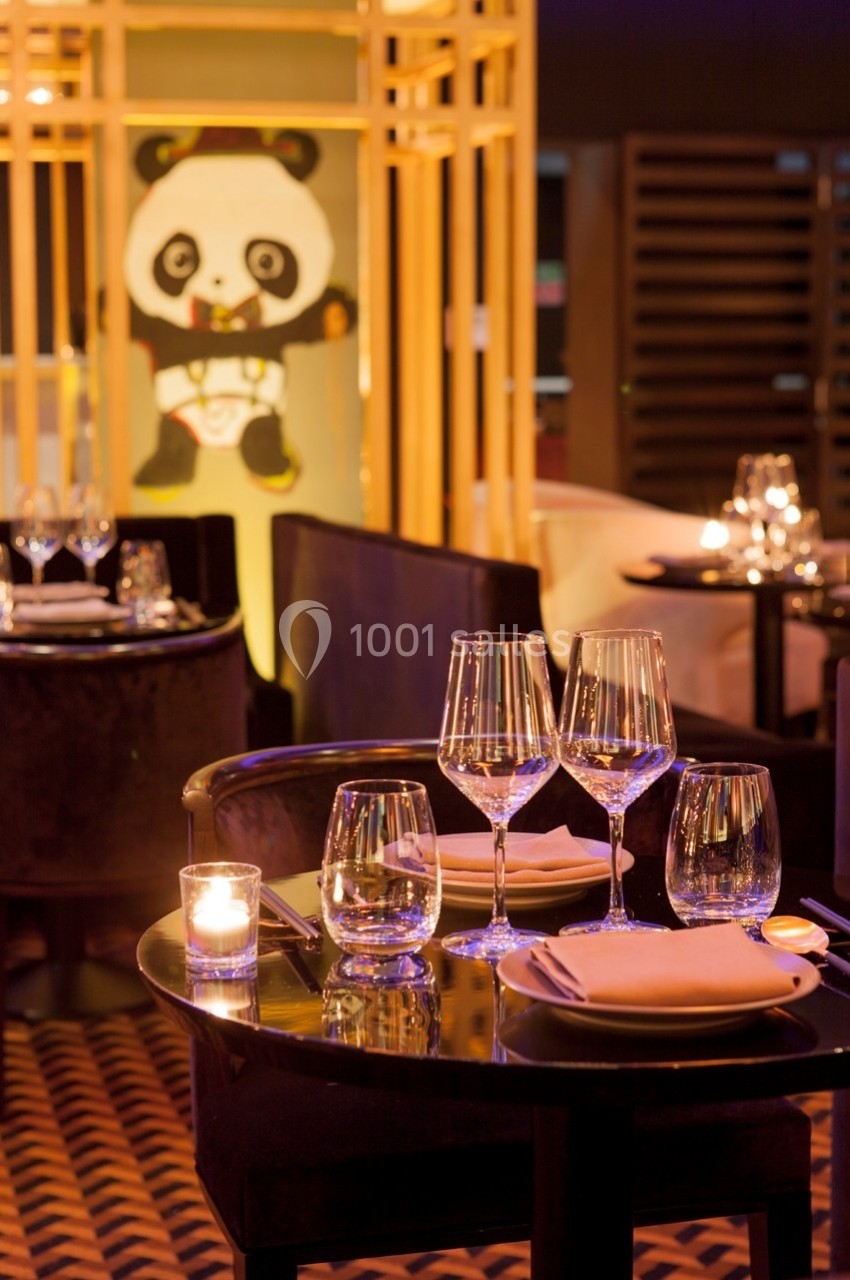 Table de restaurant élégamment dressée avec des verres et des bougies, décor intérieur avec un motif de panda en arrière…