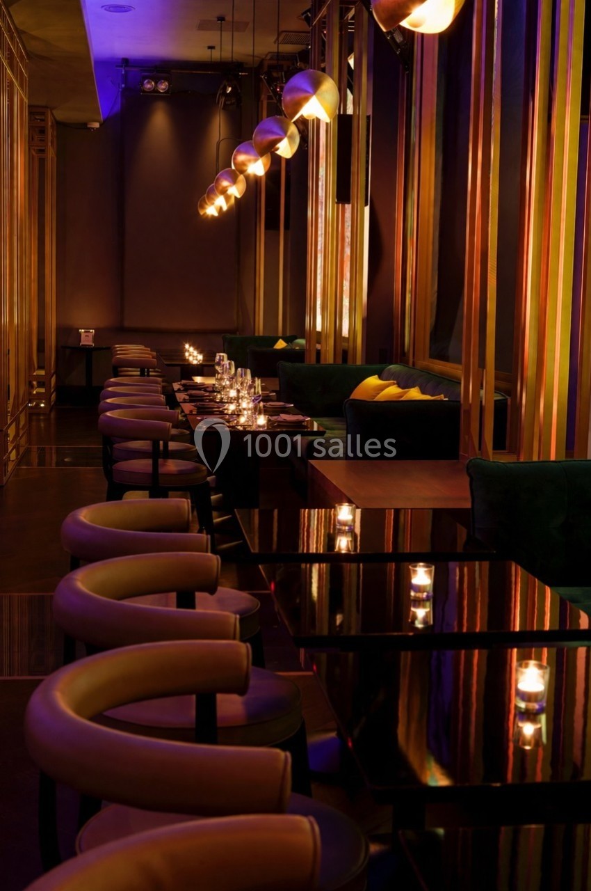 Salle de restaurant élégante avec tables noires, bougies allumées et éclairage tamisé.