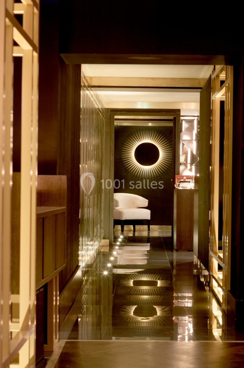 Couloir élégant avec éclairage tamisé, sol brillant et décoration murale en forme de soleil lumineux au fond.