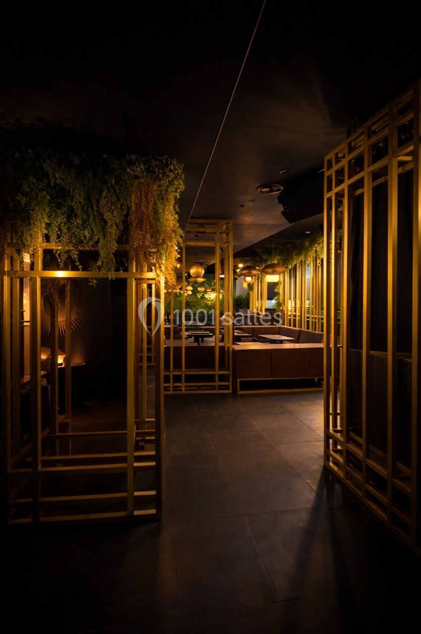 Intérieur sombre avec structures dorées, végétation suspendue et éclairage tamisé créant une ambiance chaleureuse.