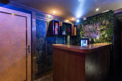 Entrée d'un espace intérieur décoré de plantes, avec un comptoir éclairé et un néon indiquant ’Gaio makes you fly’.