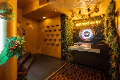 Entrée d'un espace intérieur décoré de plantes, avec un comptoir éclairé et un néon indiquant ’Gaio makes you fly’.