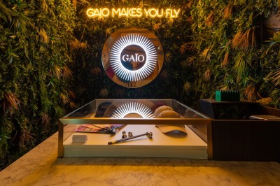 Entrée d'un espace intérieur décoré de plantes, avec un comptoir éclairé et un néon indiquant ’Gaio makes you fly’.