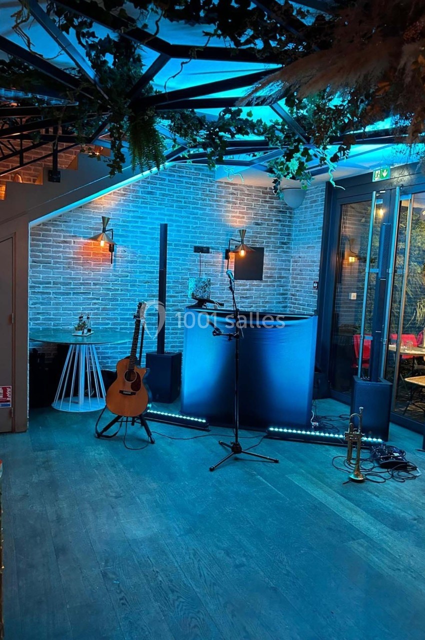 Espace intérieur avec scène équipée d'un micro, d'une guitare et d'un éclairage bleu, prêt pour une performance musicale.