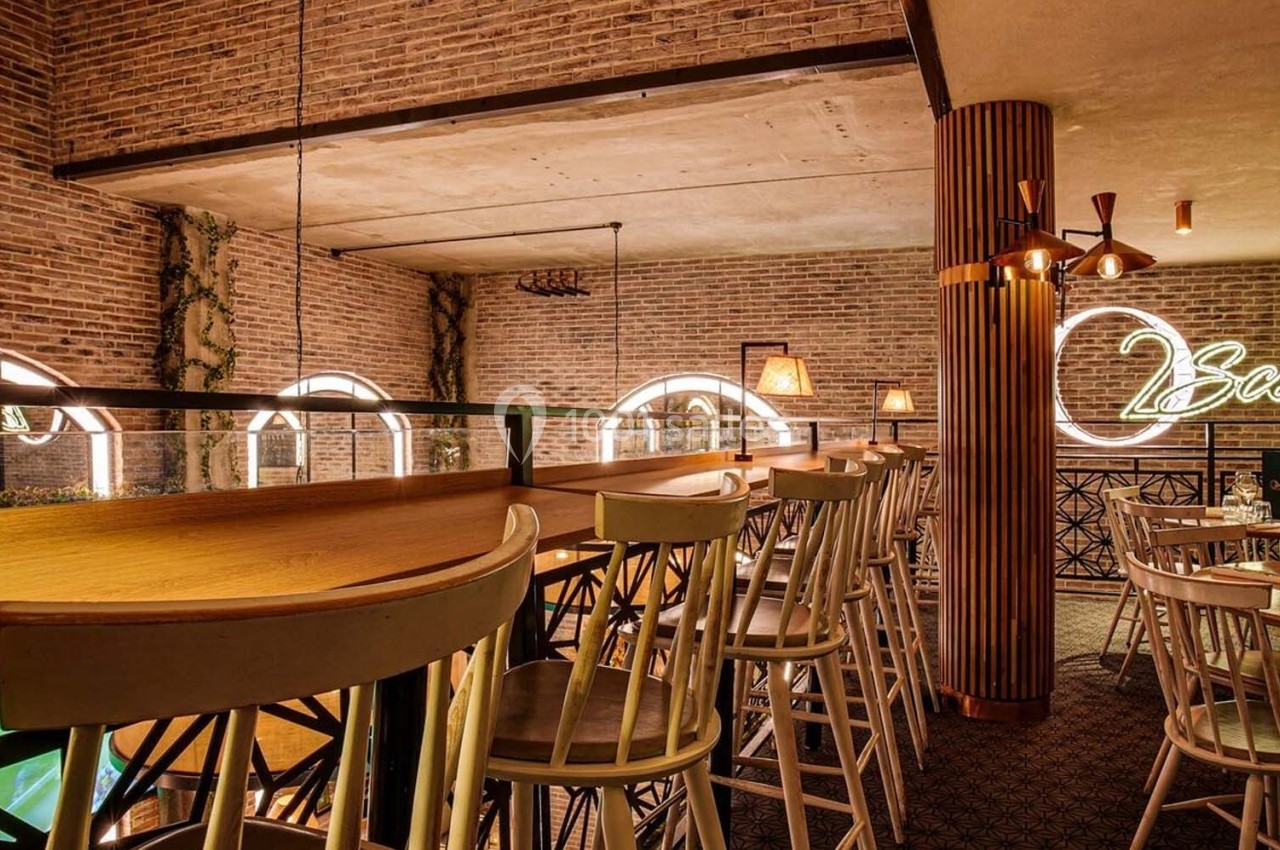 Salle de restaurant avec murs en briques, chaises hautes en bois, éclairage chaleureux et enseigne lumineuse ’Scènes’.